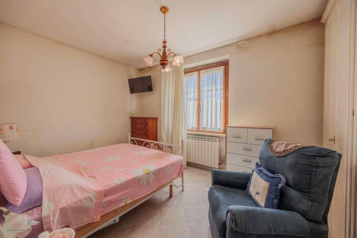 Schlafzimmer mit Einzelbett, Fliesenboden, einem Sessel und einem Fenster mit Vorhängen.
