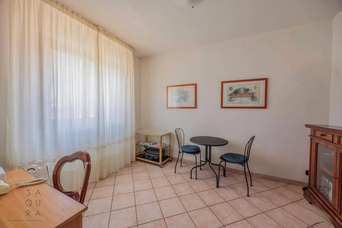Kleines Arbeitszimmer mit Fliesenboden, Fenster und einfacher Möblierung.