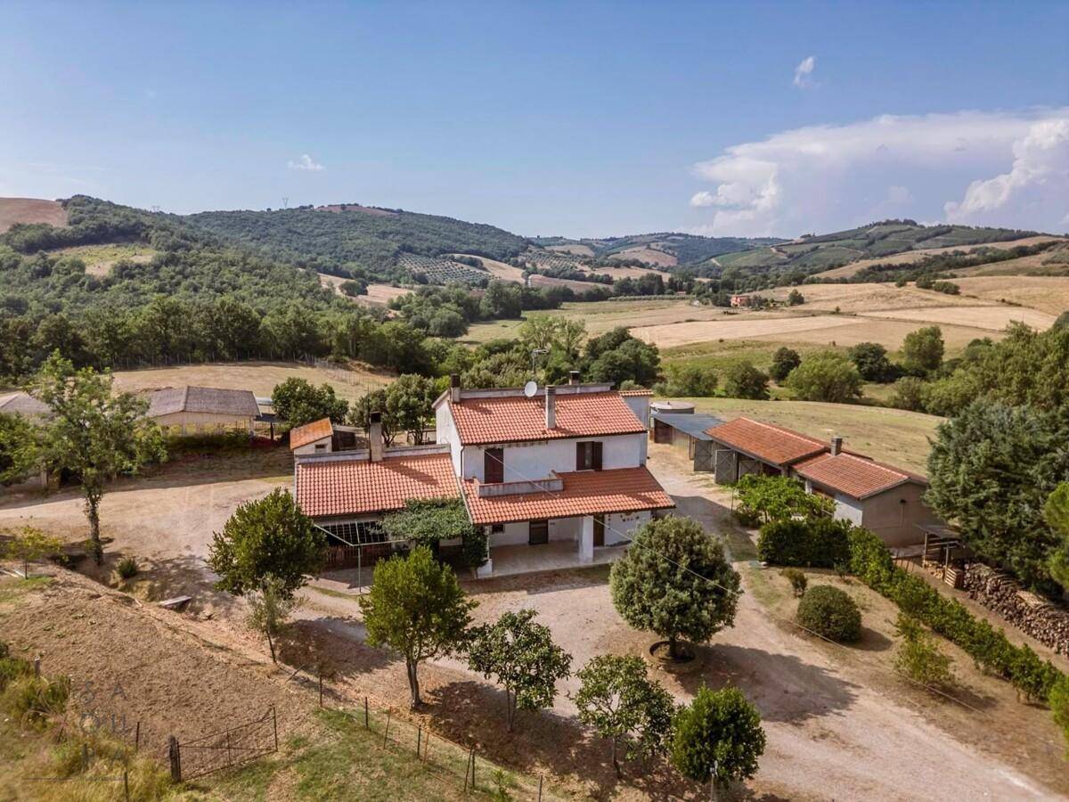Panoramablick auf das Landhaus mit seinen Nebengebäuden, eingebettet in eine hügelige Landschaft.