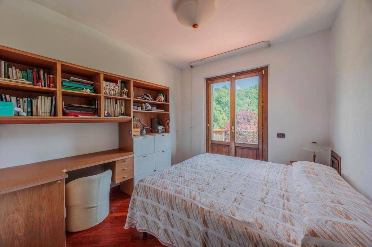 Schlafzimmer mit Holzboden, Schreibtisch, Bücherregal und Balkonzugang.