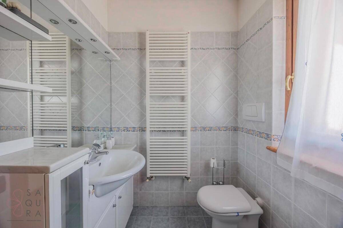 Badezimmer mit hellgrauen Fliesen, Einzelwaschbecken, Toilette und beheiztem Handtuchhalter.