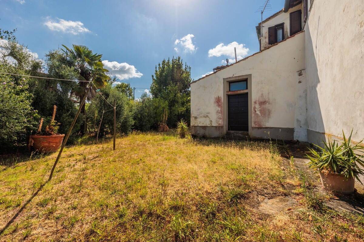 Hinterer Gartenbereich des Landhauses mit trockener Rasenfläche und Palmen im Hintergrund.