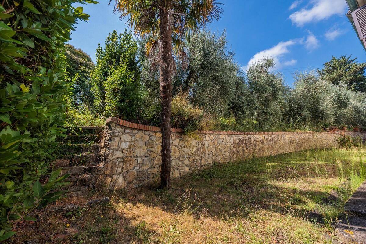 Rustikale Steinmauer im Garten mit Palmen und mediterraner Vegetation.