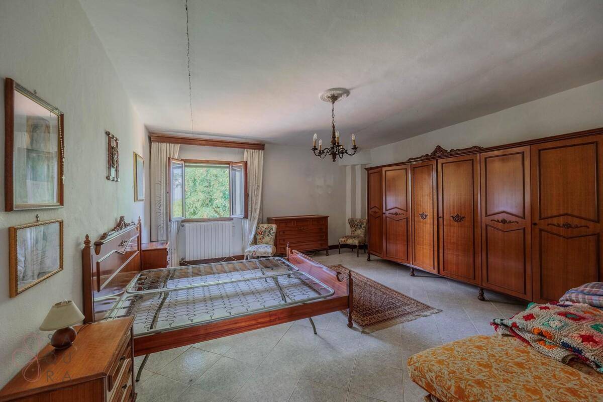 Geräumiges Schlafzimmer mit traditionellen Holzmöbeln, Fliesenboden und Blick ins Grüne.