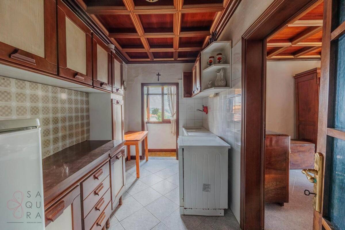 Traditionelle Küche mit Holzschränken, Fliesenboden und einem Fenster mit Ausblick.