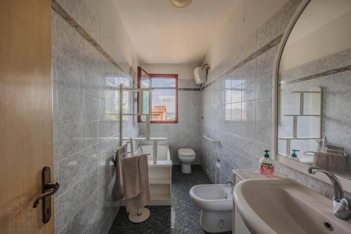 Helles Badezimmer mit grauen Fliesen, Einzelwaschbecken, WC und Bidet.