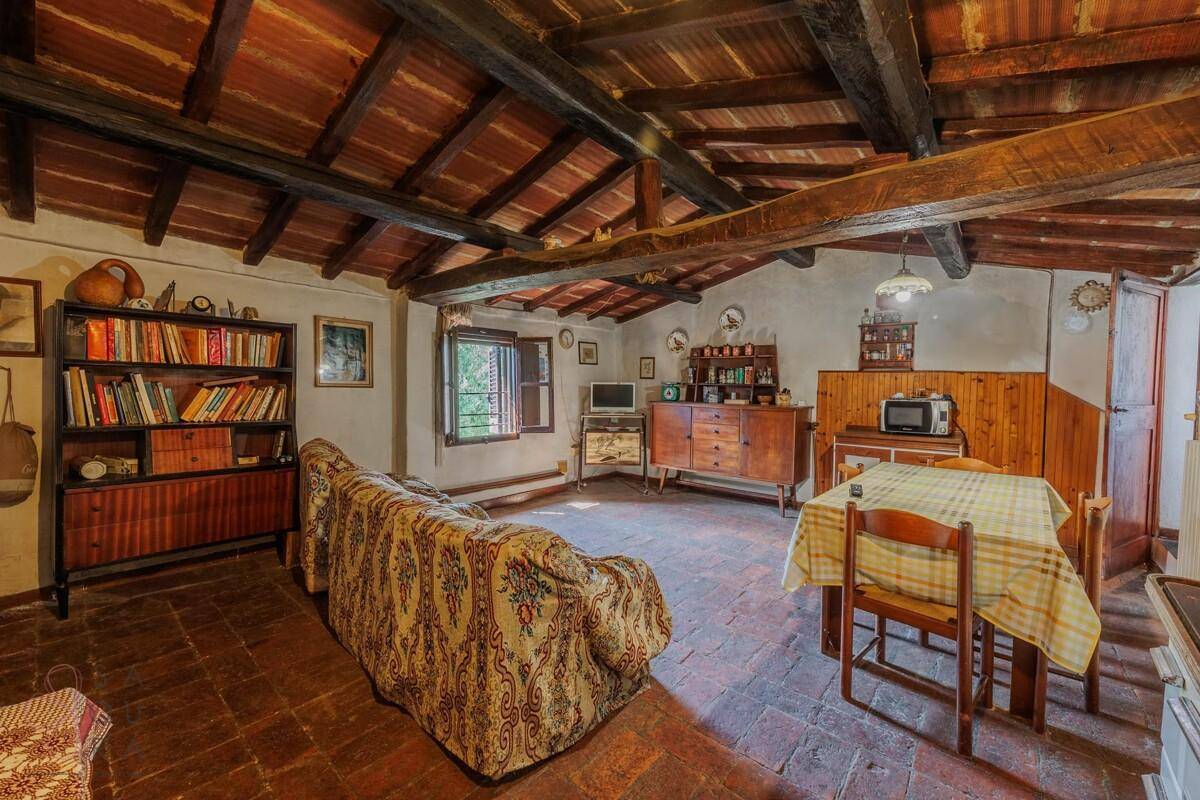 Rustikaler Wohn-Essbereich mit Holzbalkendecke, Terrakottaboden und einem Bücherregal.