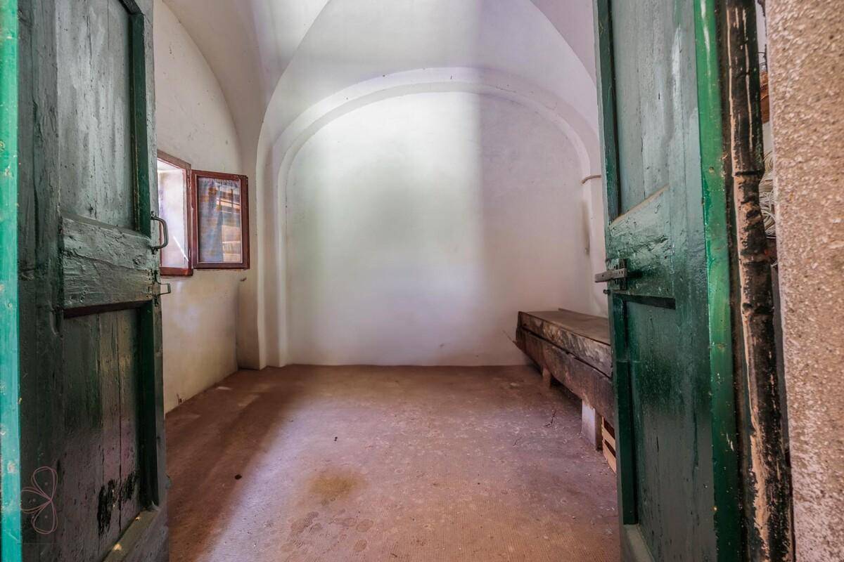 Gewölbter Raum mit weißen Wänden, Betonboden und kleinen Holzfenstern, durch große Türen zugänglich.