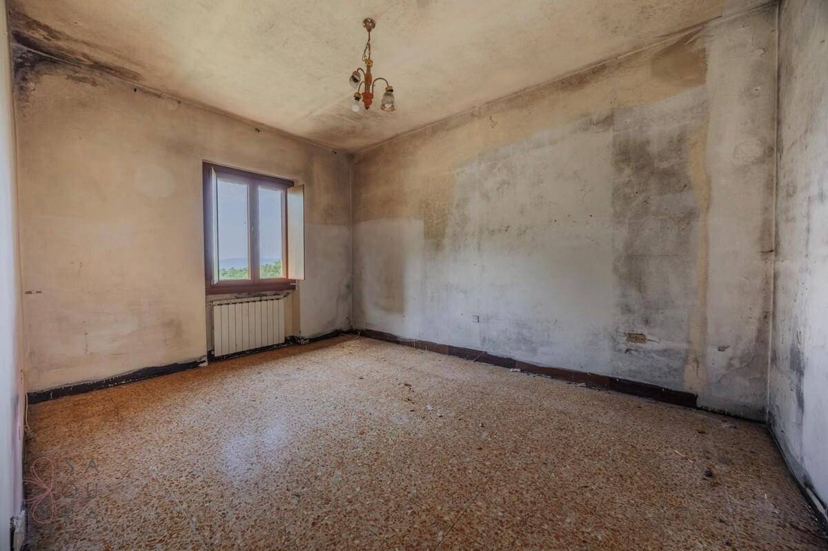 Leerer Raum mit Terrazzoboden und Fenster, die Wände zeigen deutliche Gebrauchsspuren.