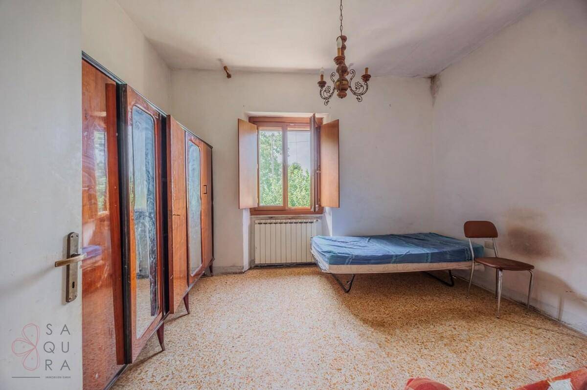Schlafzimmer mit Terrazzoboden, Einzelbett und Holzschrank, mit Blick ins Grüne.