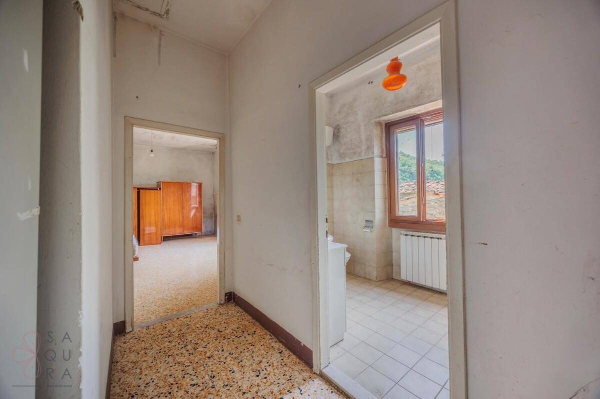 Flur mit Terrazzoboden, der zu verschiedenen Räumen führt, darunter ein Badezimmer.