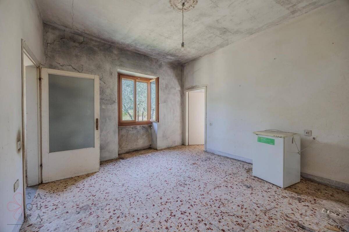 Leerer Raum mit Terrazzoboden und Fenster, die Wände zeigen deutliche Gebrauchsspuren.