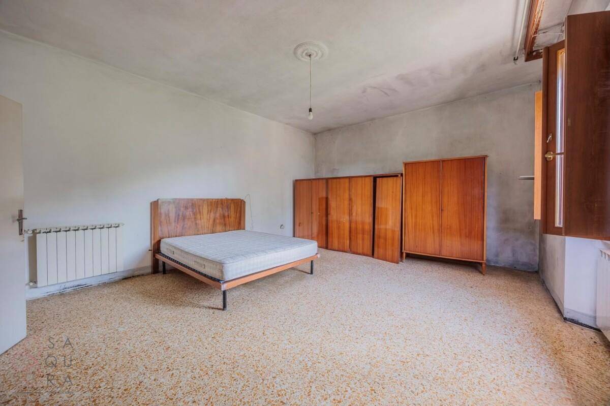 Geräumiges Schlafzimmer mit Terrazzoboden, Doppelbett und Holzschränken, renovierungsbedürftig.