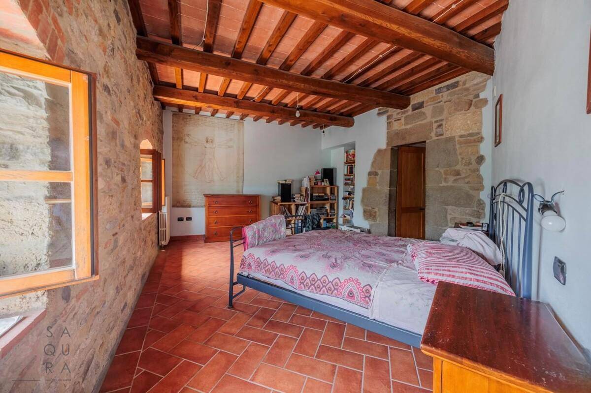 Gemütliches Schlafzimmer mit freiliegenden Steinwänden, Holzbalkendecke und Terrakottaboden.
