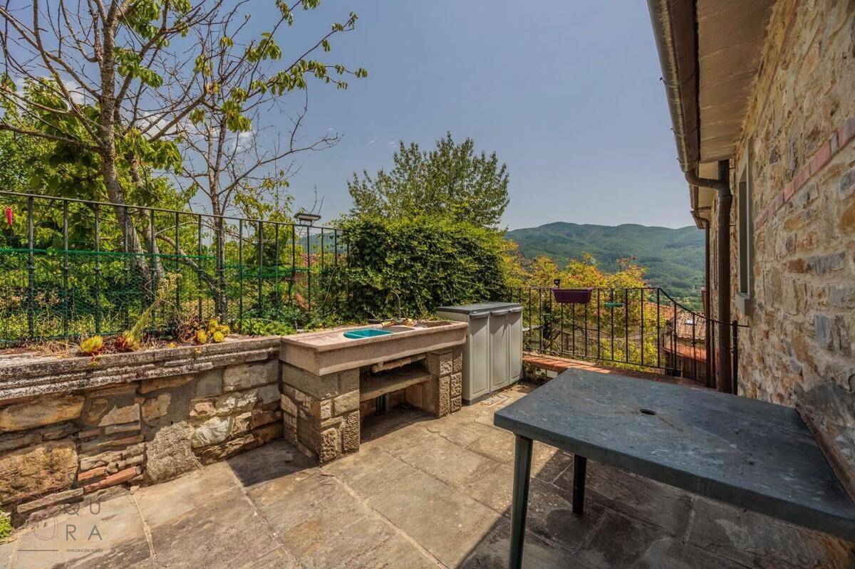 Sonniger Außenbereich mit Steinterrasse, eingebautem Grill und weitem Blick auf die Landschaft.