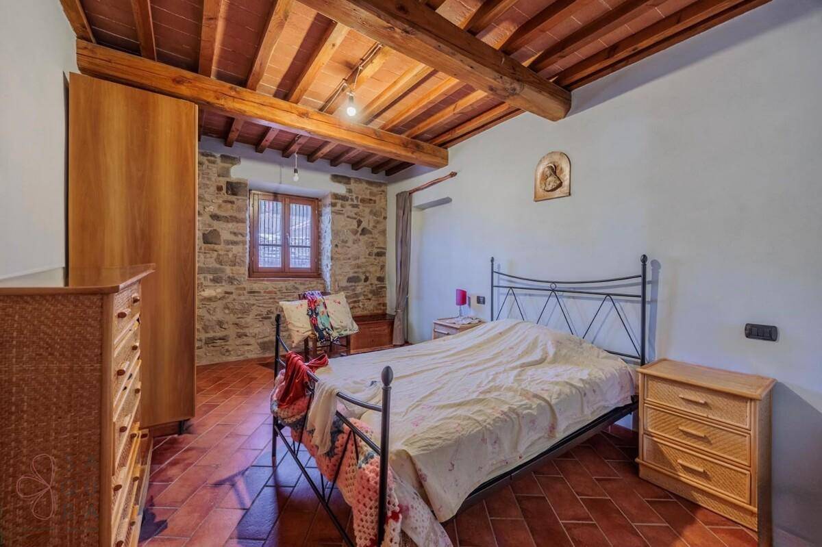 Rustikales Schlafzimmer mit Holzbalkendecke, Steinwand und Terrakottaboden, ausgestattet mit Holzmöbeln.