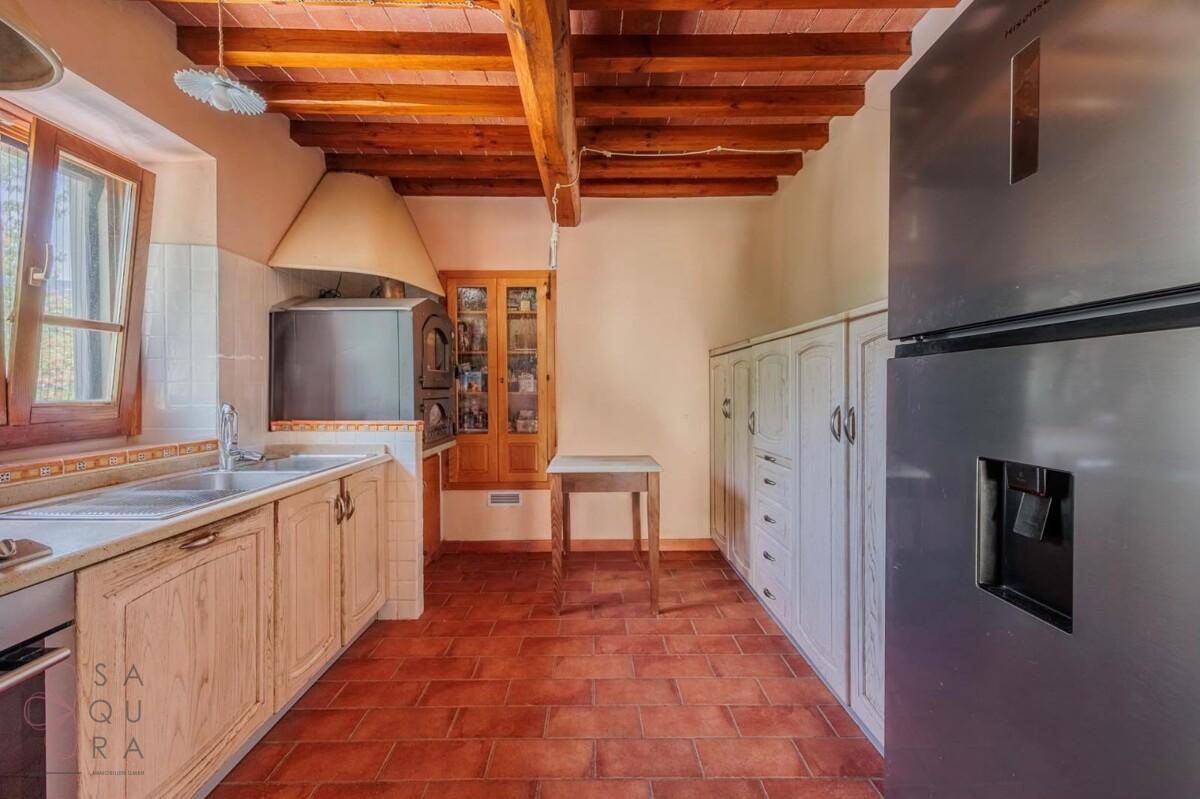 Traditionelle Küche mit Holzbalkendecke, Terrakottaboden und einfachen Holzschränken.
