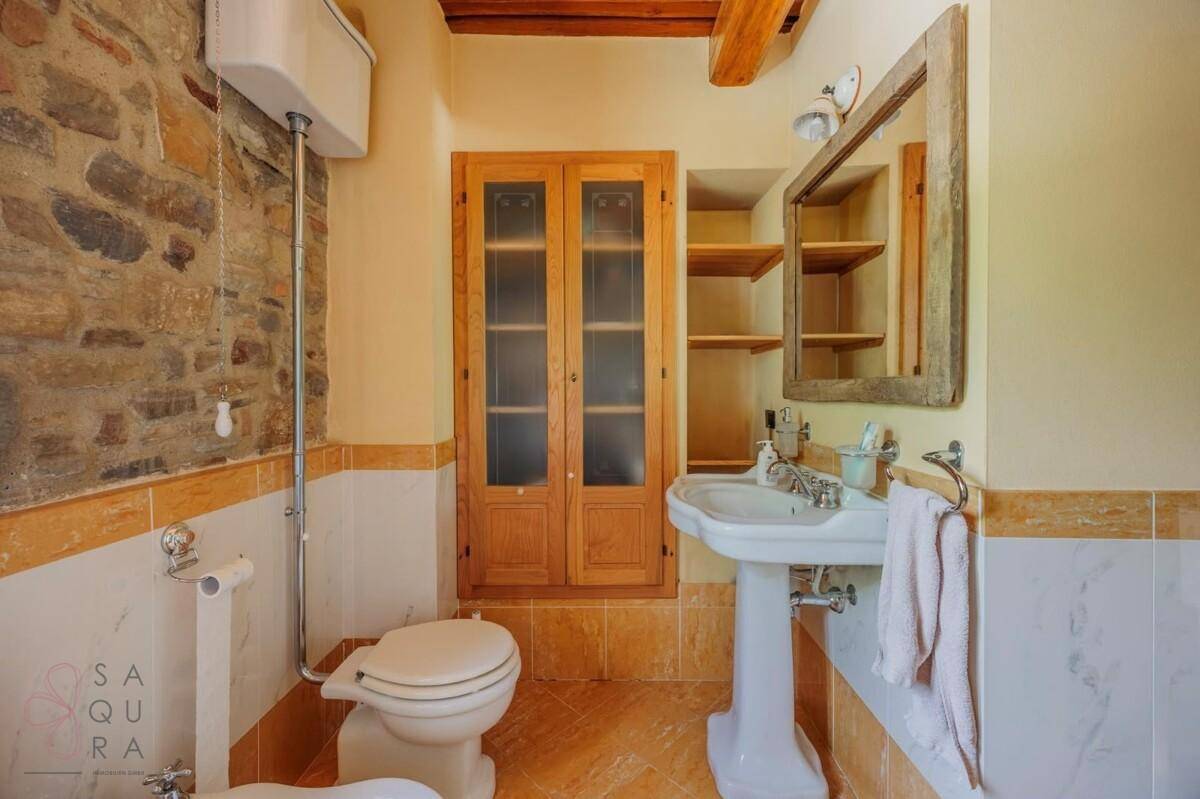Badezimmer mit Waschtisch, Spiegel und WC, ergänzt durch eine freiliegende Steinwand.
