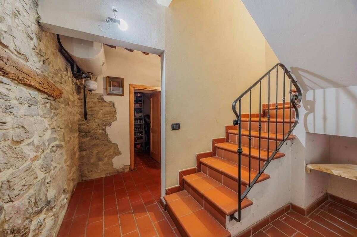 Flur mit Terrakottaboden, freiliegender Steinwand und einer Treppe mit schmiedeeisernem Geländer.