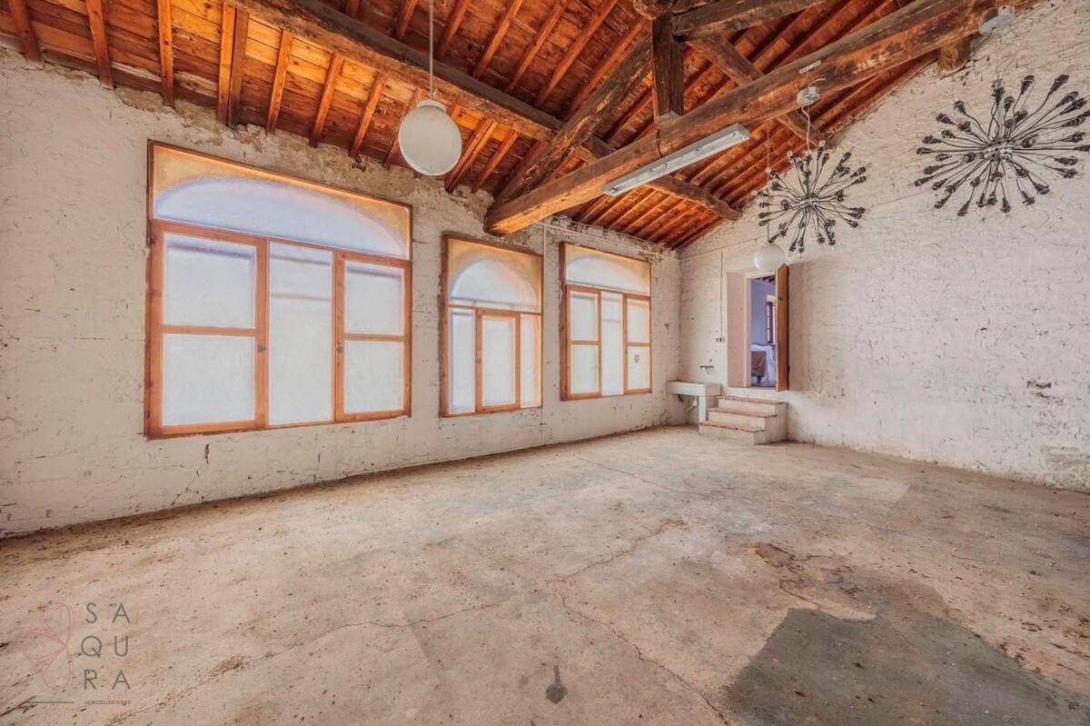 Großer leerer Raum mit freiliegenden Holzbalken, Ziegelwänden und Betonboden.