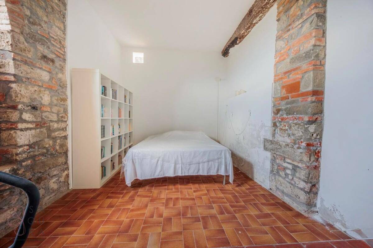 Kleines Schlafzimmer mit Bücherregal, freiliegenden Steinwänden und Terrakottaboden.