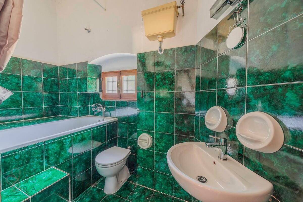 Badezimmer mit grünen Fliesen, Badewanne, Bidet und Fenster.