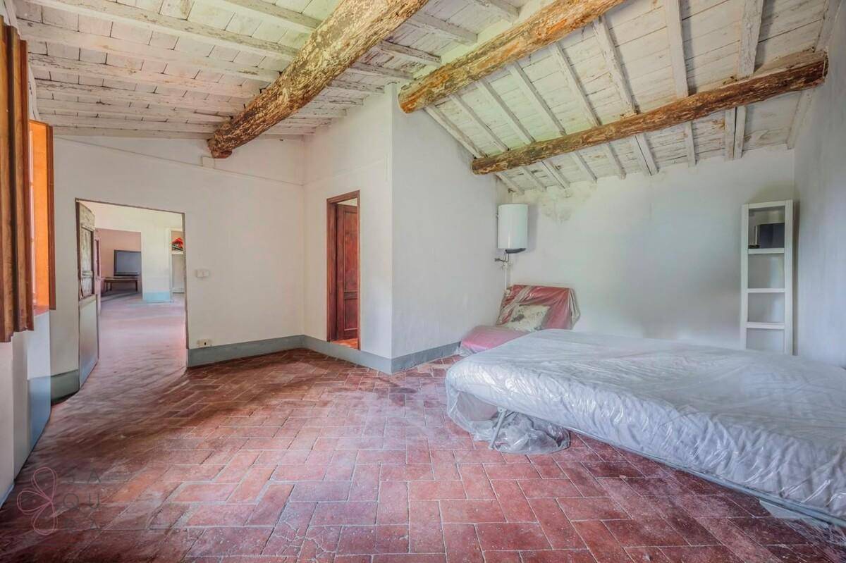 Geräumiges Schlafzimmer mit freiliegenden Holzbalken, schrägen Decken und Terrakottaboden.