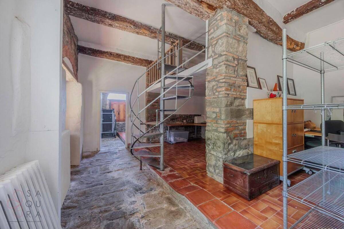 Innenraum mit Wendeltreppe, freiliegenden Steinwänden und Terrakottaboden.