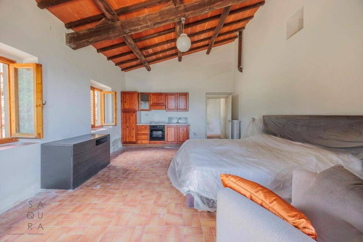 Schlafzimmer mit integrierter Küchenzeile, freiliegenden Holzbalken und Terrakottaboden.