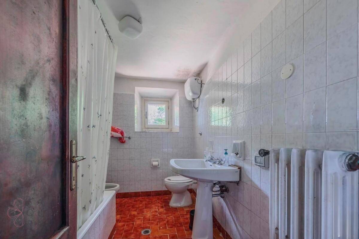 Badezimmer mit weißen Fliesen, Badewanne, Fenster und Heizkörper.