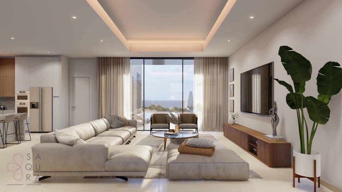 Heller Wohnbereich mit großem Sofa, Meerblick und offener Küche im Hintergrund.