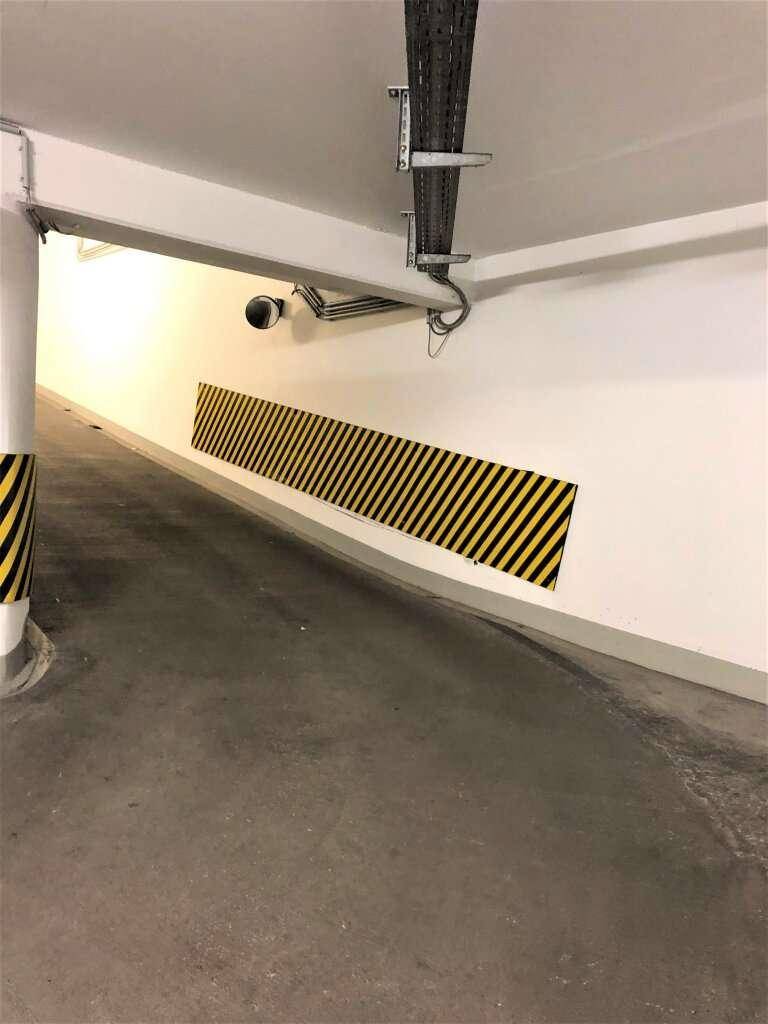 Zufahrtsrampe zur Tiefgarage mit Sicherheitskamera, Kabeltrassen und Warnmarkierungen an der Wand.