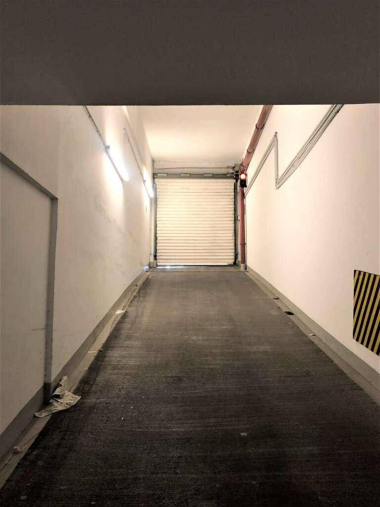 Einfahrt zur Tiefgarage mit geschlossener Rolltor, Beleuchtung und Warnmarkierungen an der Seite.