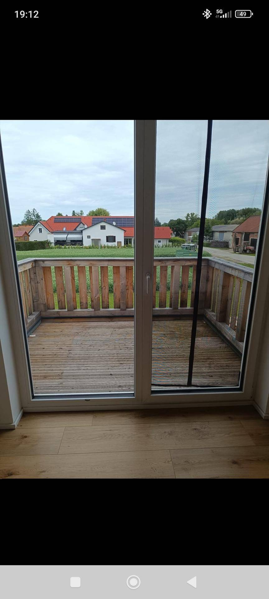 Geräumiger Holzbalkon mit Blick auf die umliegende Wohnsiedlung und grüne Umgebung.