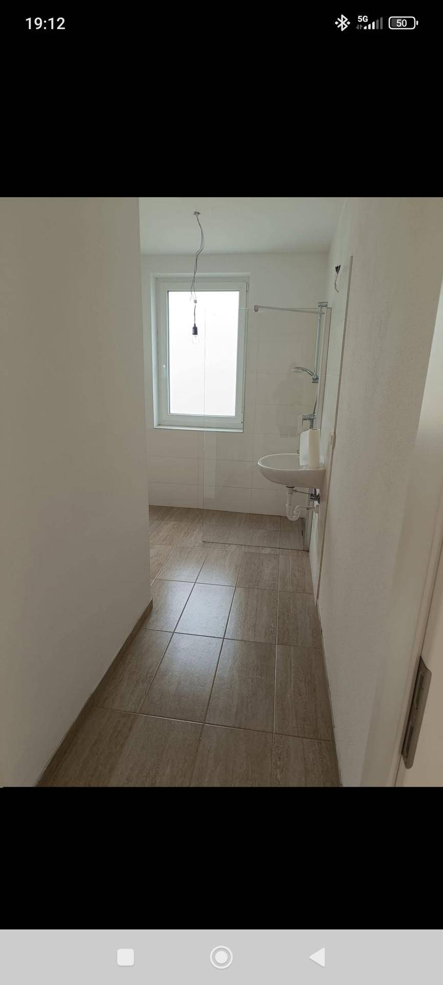 Heller Flur mit Fliesenboden, der zu einem Badezimmer mit Fenster führt.