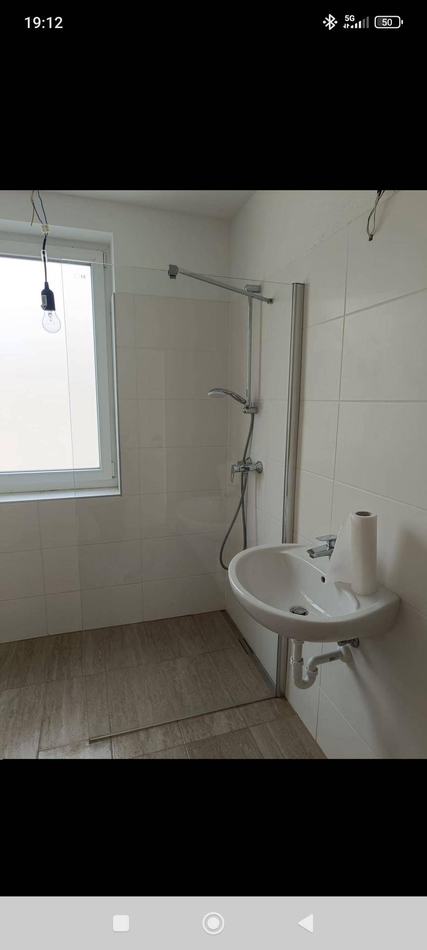 Modernes Badezimmer mit Duschkabine, Waschbecken und Fenster, hell gefliest.