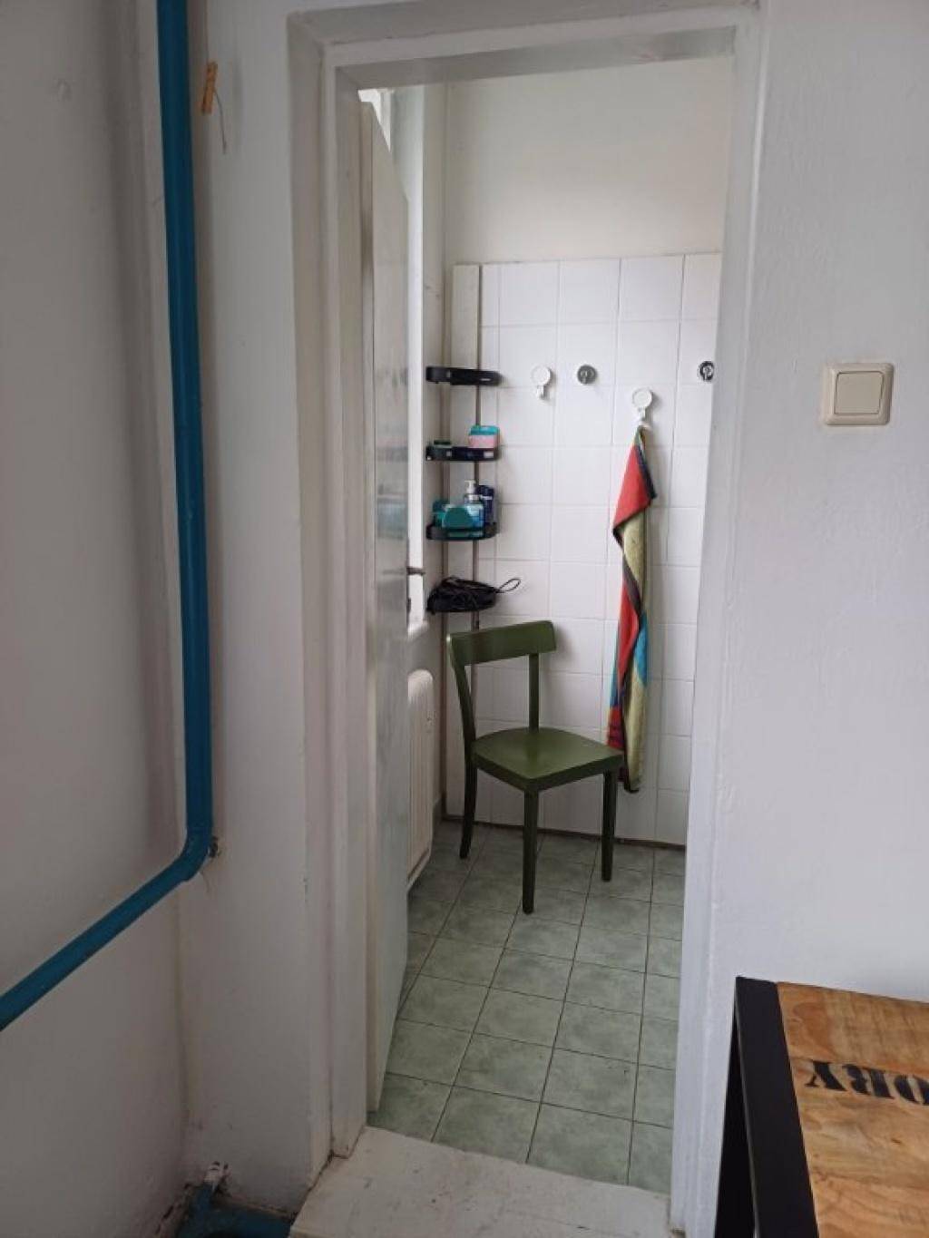 Blick in ein kleines Badezimmer mit Fliesenboden und einem grünen Stuhl.