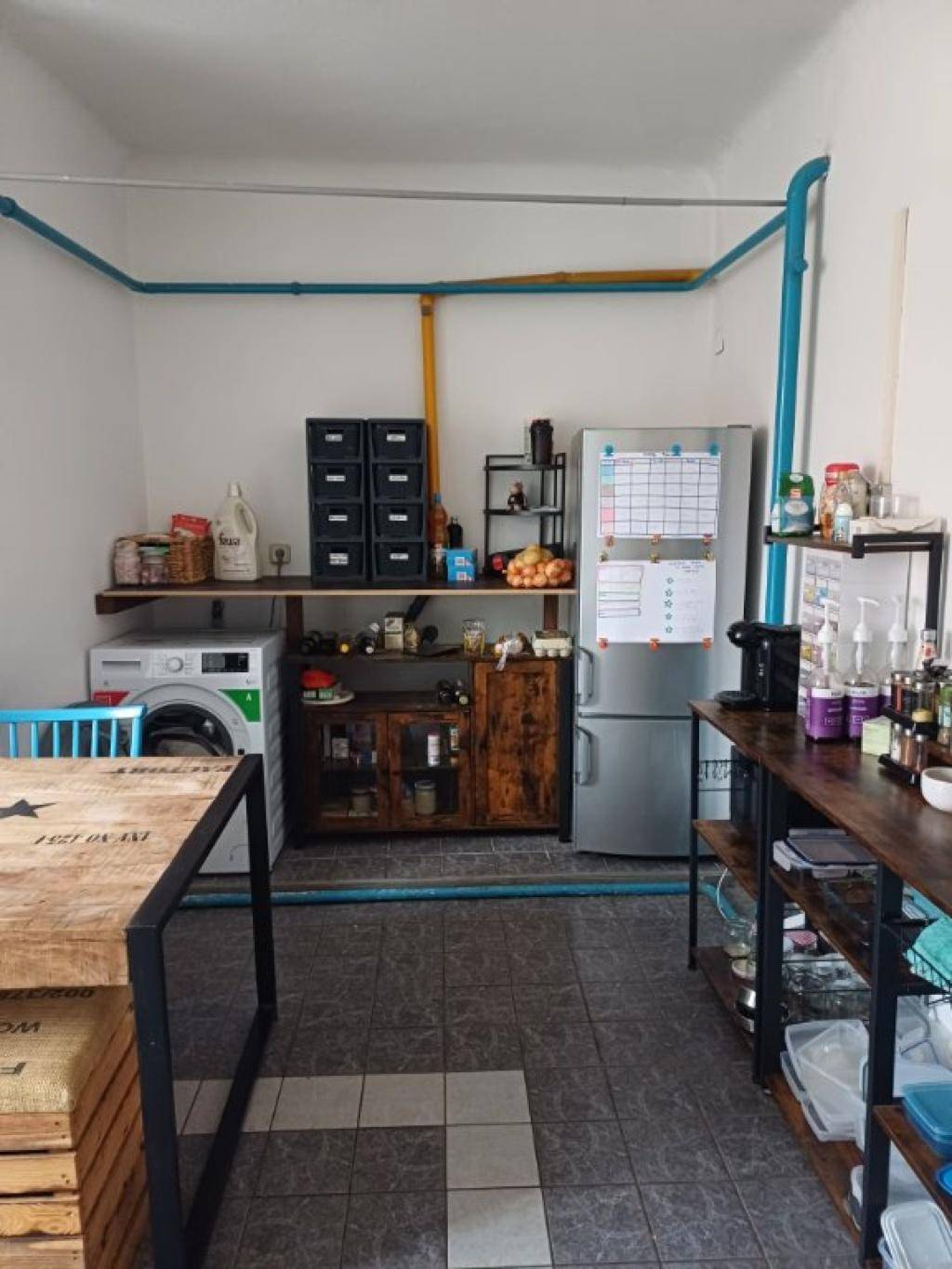 Geräumige Küche mit Waschmaschine, Kühlschrank und sichtbaren Installationen.