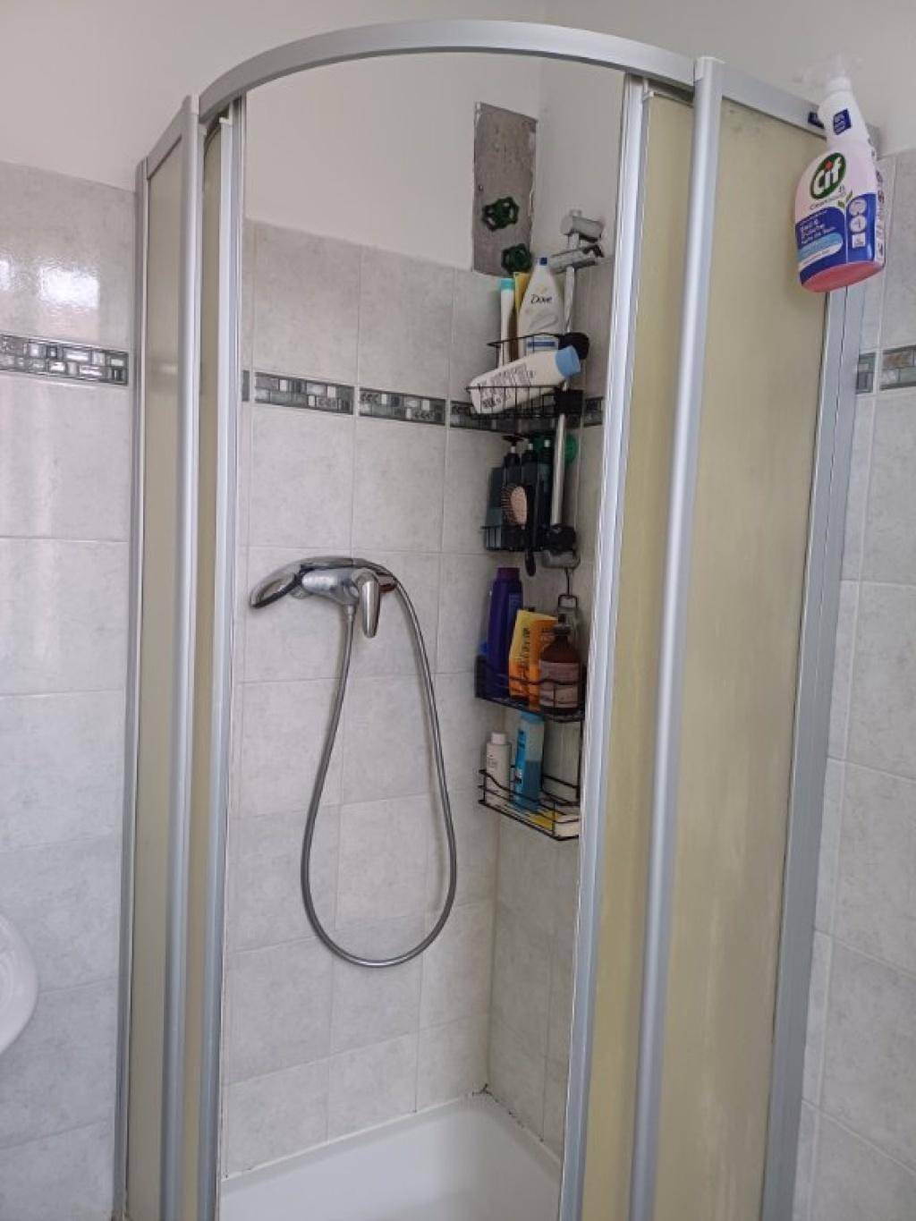 Duschkabine mit Fliesenwänden und Duscharmatur in einem einfachen Badezimmer.
