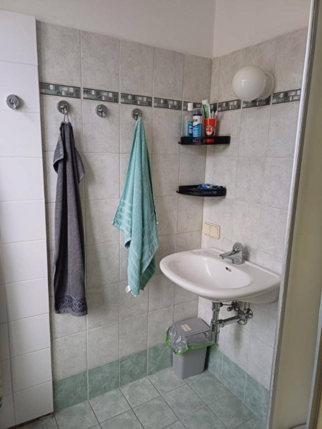 Waschbeckenbereich im Badezimmer mit Fliesen, Handtüchern und Spiegel.