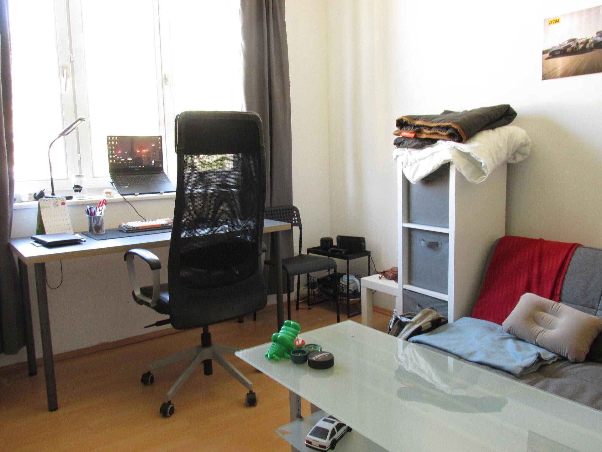 Detailansicht des Arbeitsbereichs mit Schreibtisch, Bürostuhl und Laptop am Fenster.