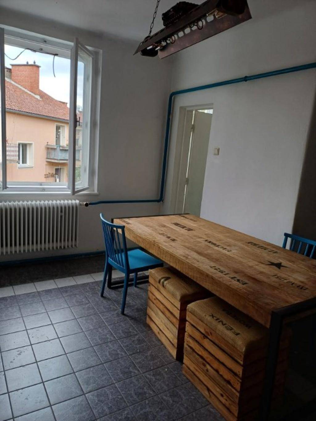 Essbereich in der Küche mit großem Holztisch und blauen Stühlen, Blick nach draußen.