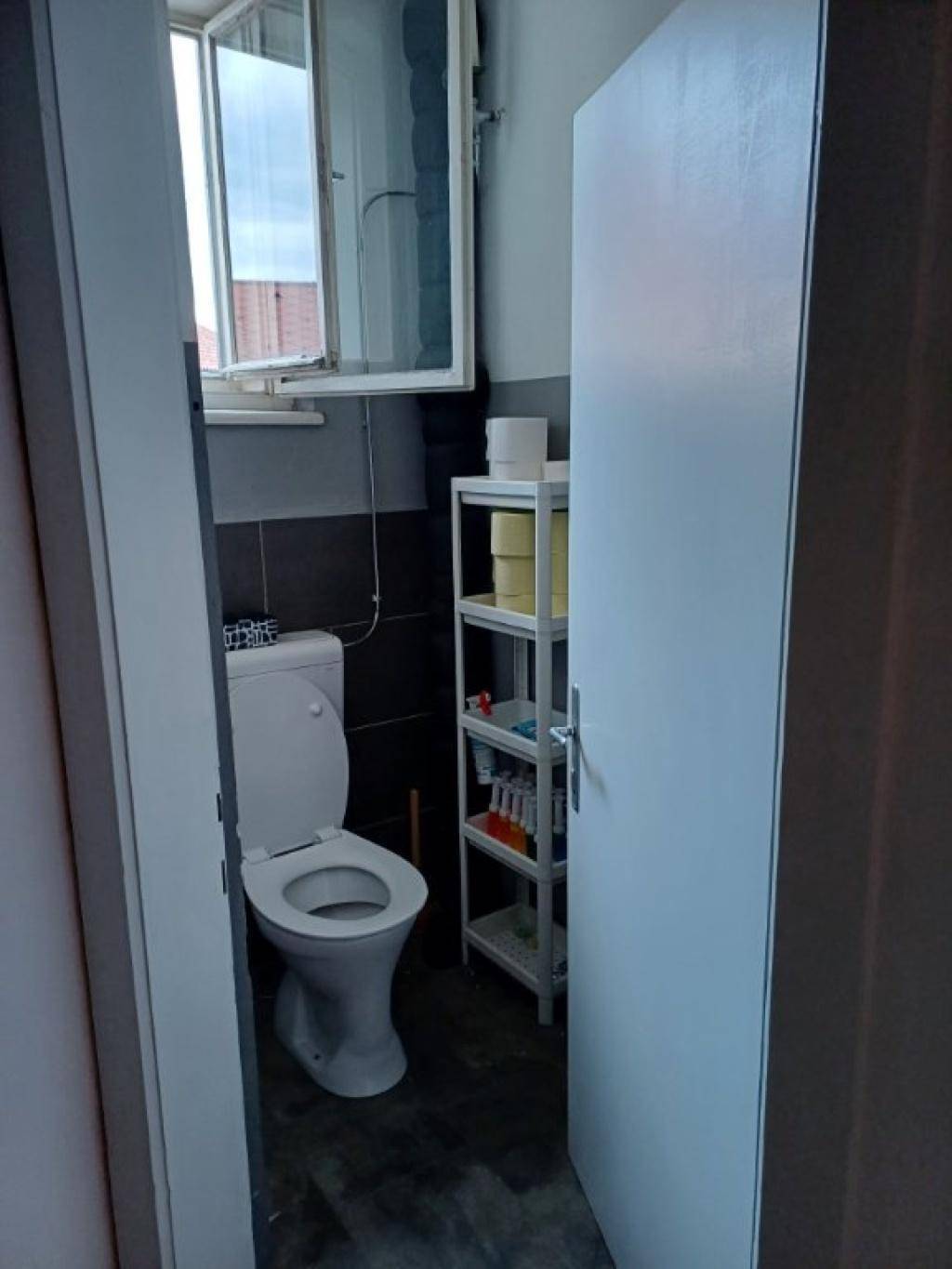 Separates WC mit Toilette, Fenster und Regal für Badutensilien.