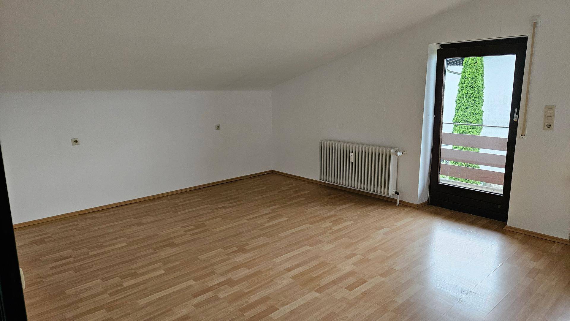 Geräumiger Wohnraum mit Laminatboden, Dachschräge und Zugang zu einem Außenbereich.