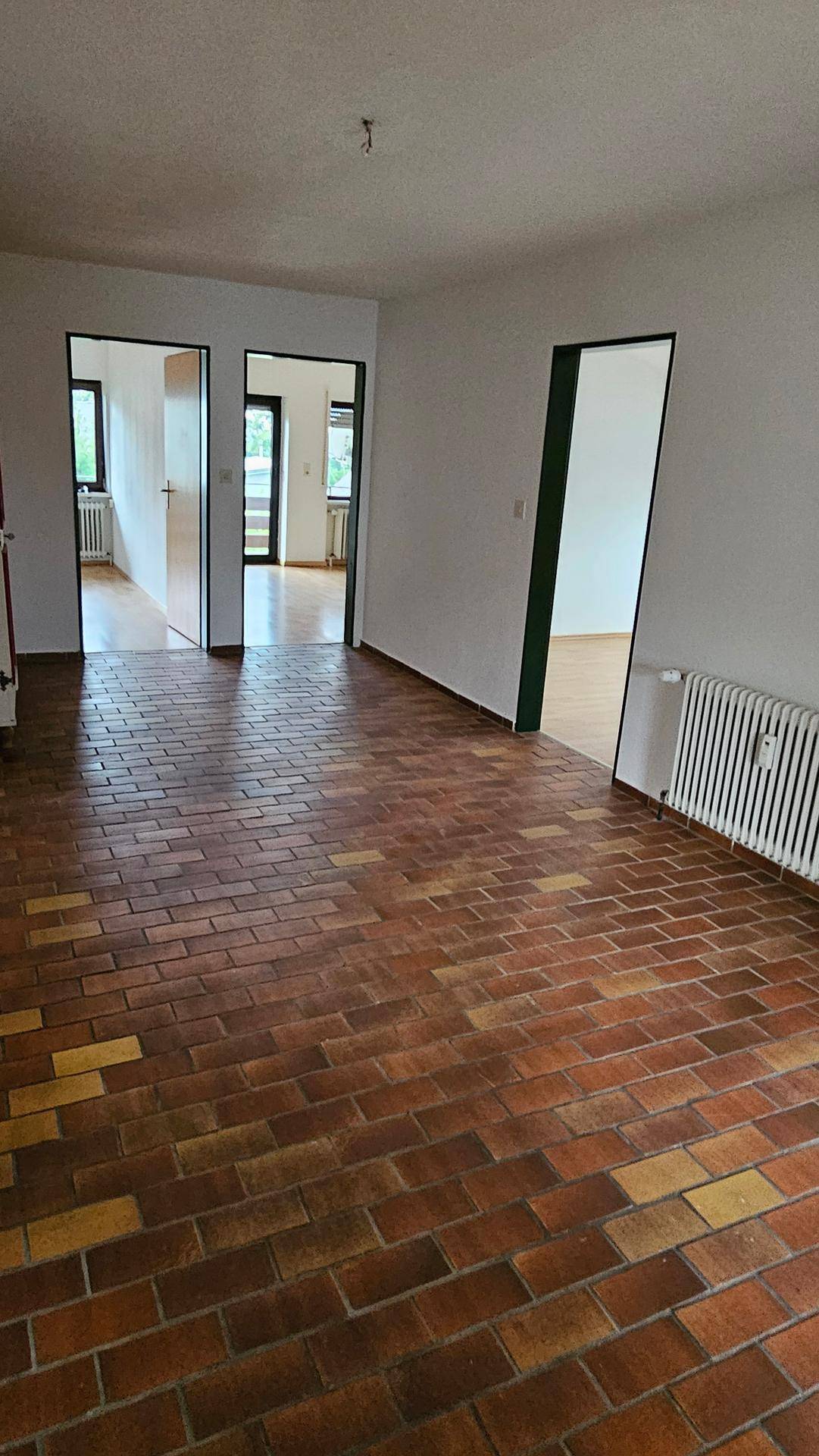 Geräumiger Raum mit Terrakotta-Fliesenboden und mehreren Türöffnungen zu anderen Zimmern.