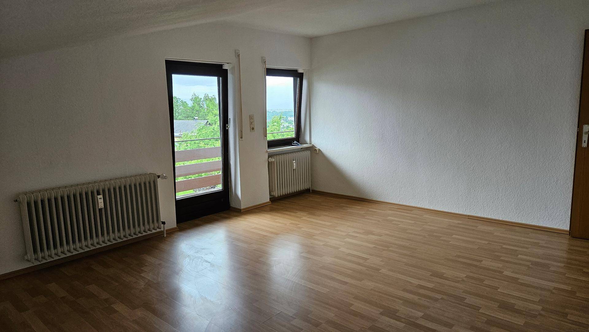 Heller Wohnraum mit Laminatboden, Dachschräge und Zugang zu Balkon oder Terrasse mit Grünblick.