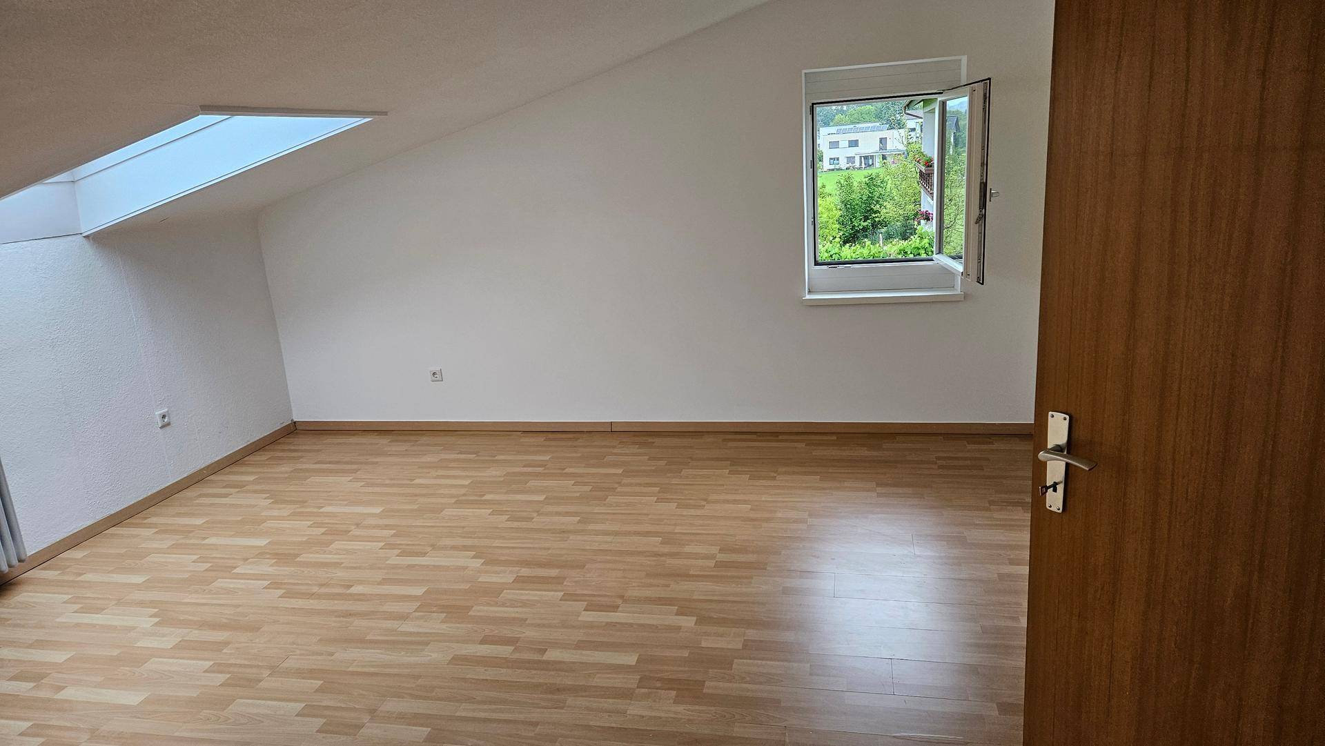 Helles Schlafzimmer im Dachgeschoss mit Laminatboden, Dachfenster und Grünblick.
