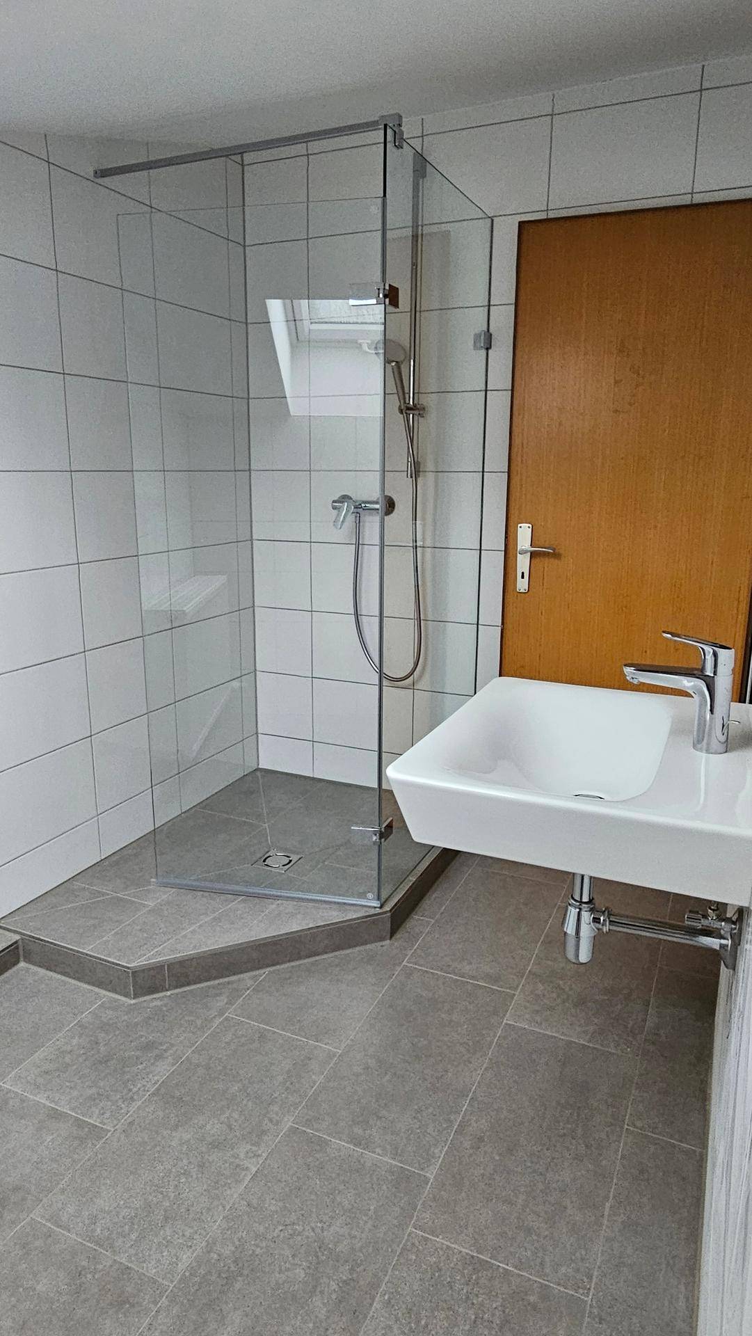 Helles Badezimmer mit moderner Glasdusche, Waschbecken und weißen Wandfliesen.