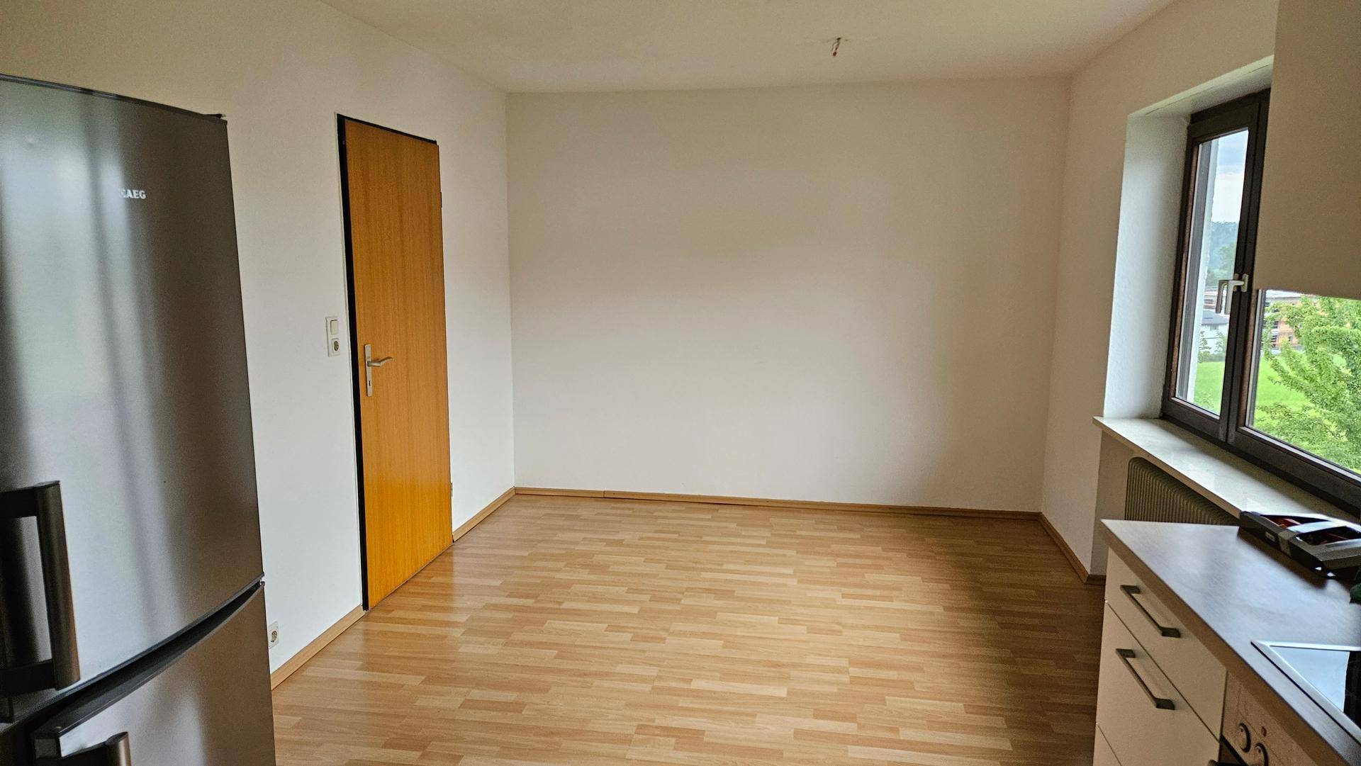 Leerer Raum mit Laminatboden, weißen Wänden und einem Fenster, ideal als Essbereich.