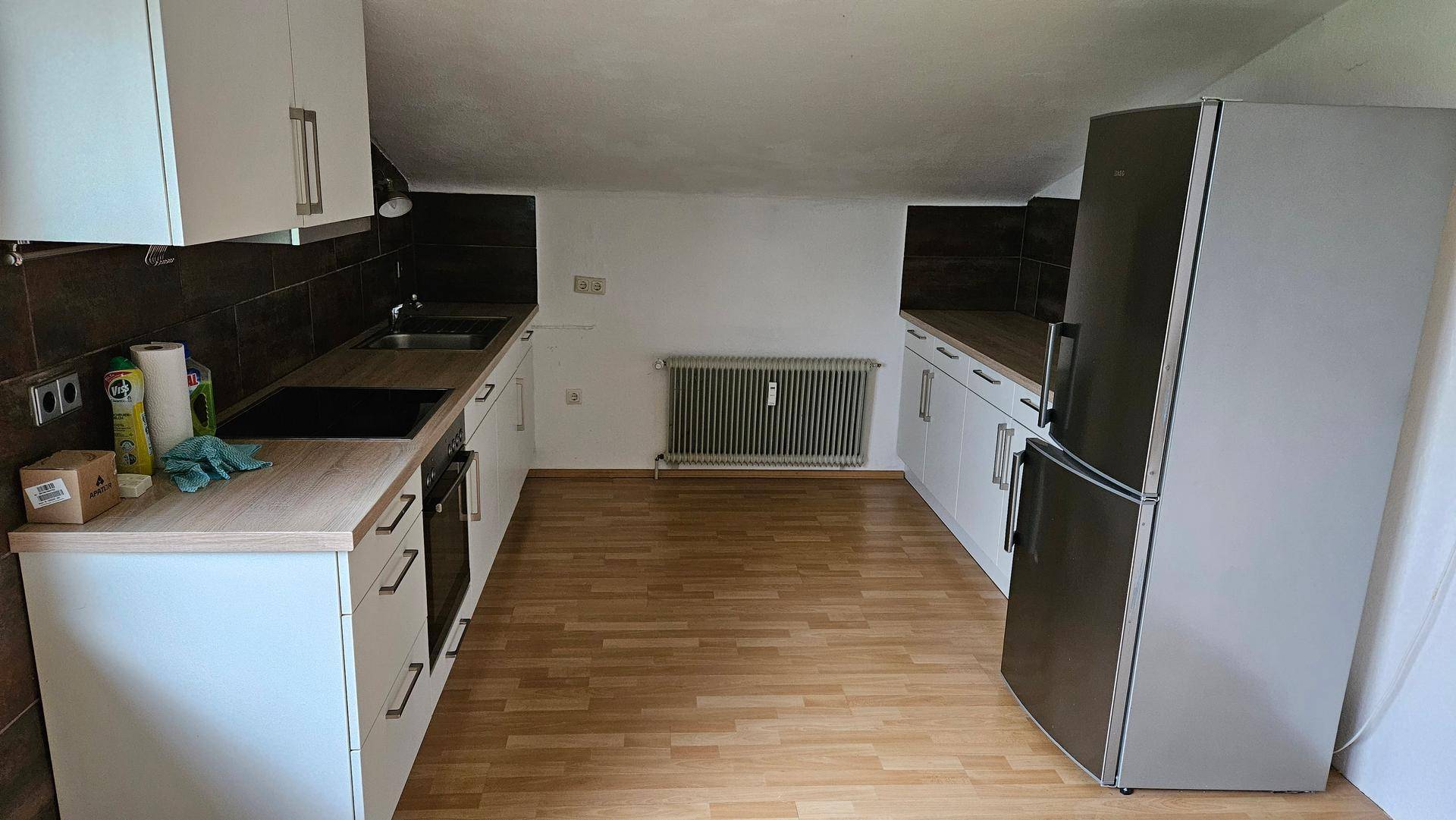 Helle Küche mit weißen Schränken, Holzarbeitsplatten, Kühlschrank und Dachschräge.